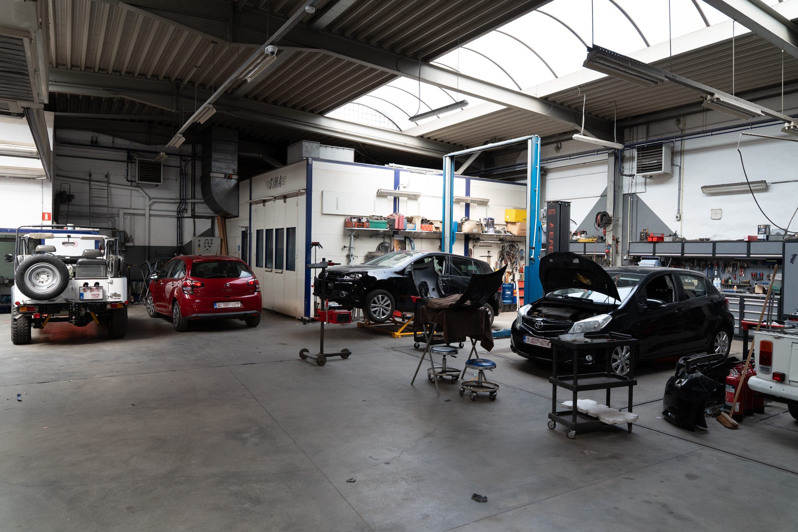 Vue générale de l’atelier Carrosserie Brosens : véhicules en réparation devant la cabine de peinture